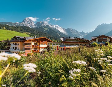 Hotelansicht des Urslaurerhofs im Sommer mit Bergkulisse und blühender Wiese.