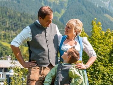 Gastgeberfamilie Kraker-Neumayr mit Kind in traditioneller Tracht vor Bergkulisse.